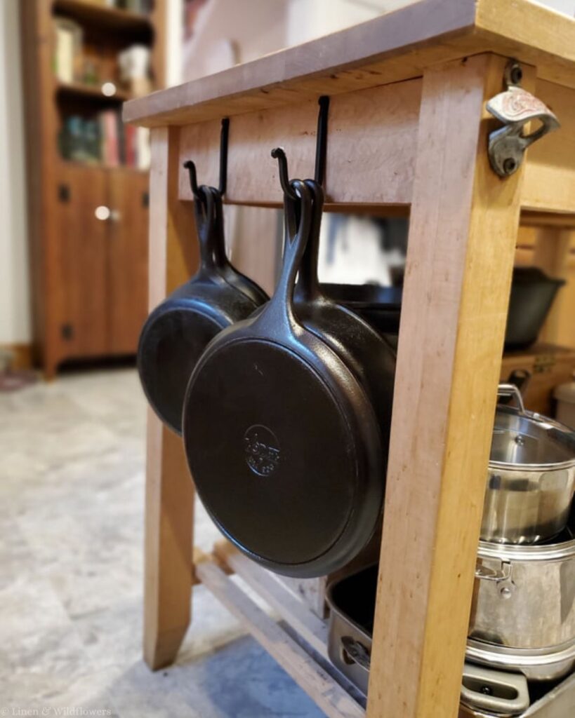 Two cast iron skillets hanging from hooks on the side of a wooden kitchen island.