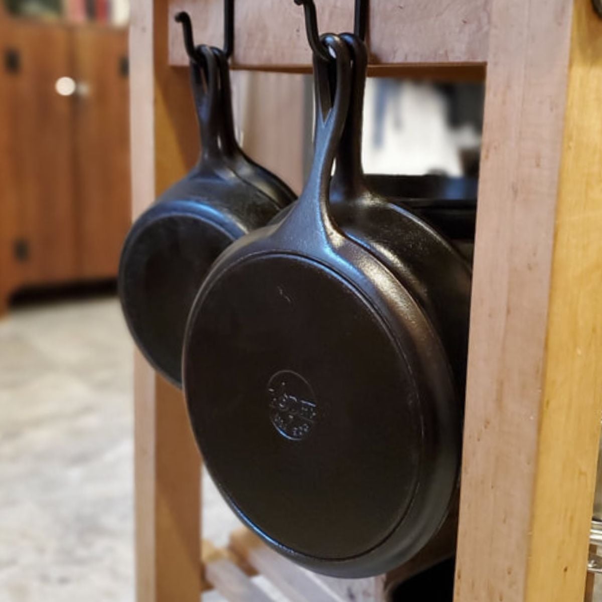 Cast iron skillets hanging from hooks on a wooden kitchen island, a practical storage idea for a cozy vintage kitchen.