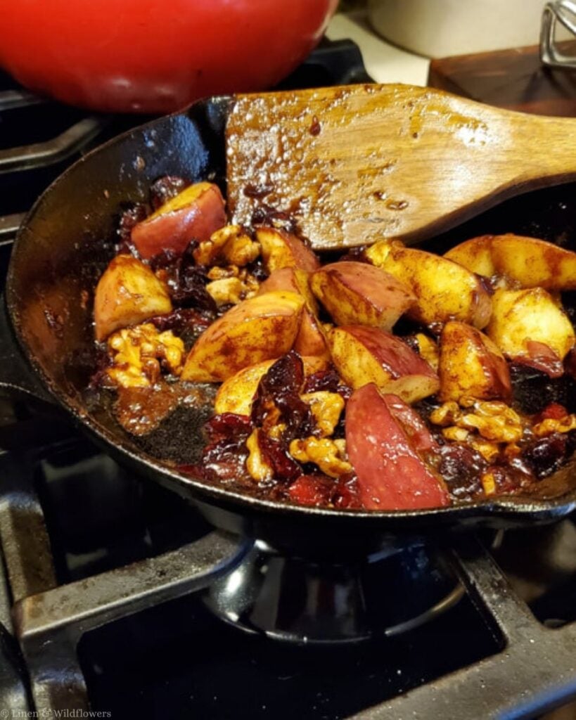 Cinnamon-spiced apples with walnuts and dried cranberries sautéing in a cast iron skillet.