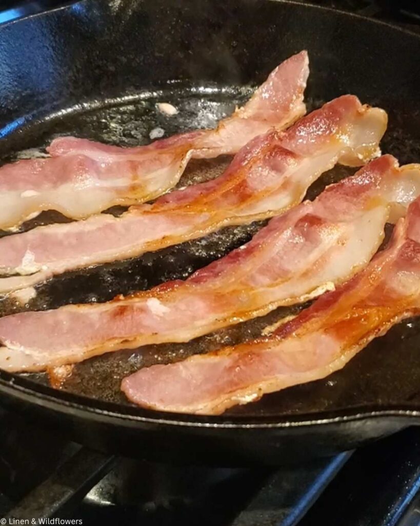 Four crispy bacon strips sizzling in a black cast-iron skillet, highlighting their golden-brown edges and glossy texture, evoking a sense of warmth.