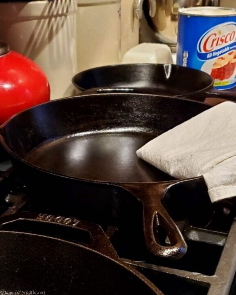 Freshly seasoned cast iron skillet on the stovetop next to a linen towel and can of Crisco shortening.