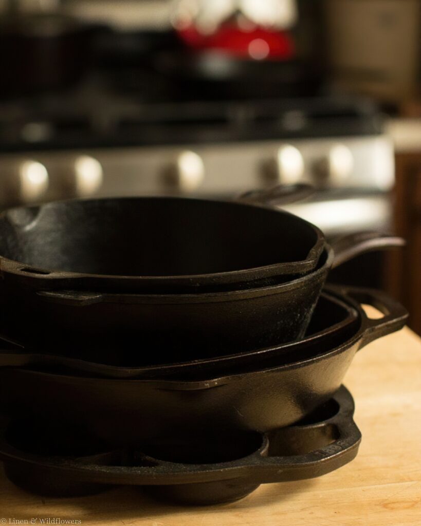 Stack of well-seasoned cast iron skillets on a wooden butcher block countertop.