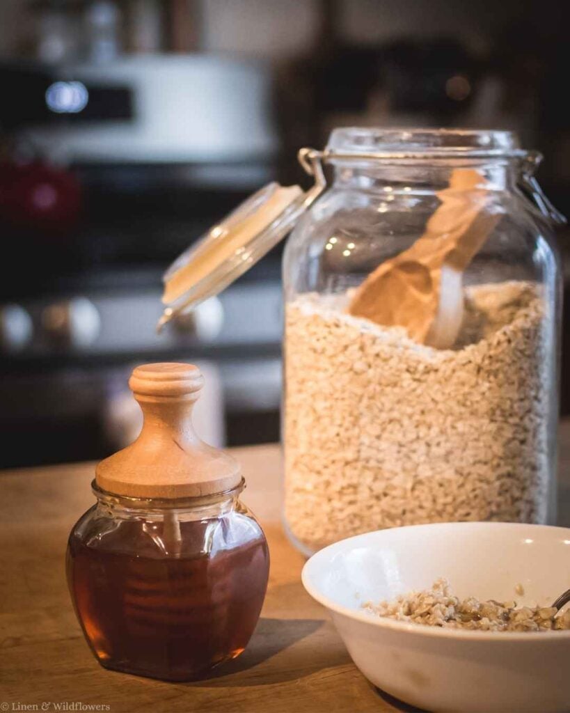 Honey jar with wooden dipper lid styled beside a jar of rolled oats and a bowl of oatmeal for pantry décor.