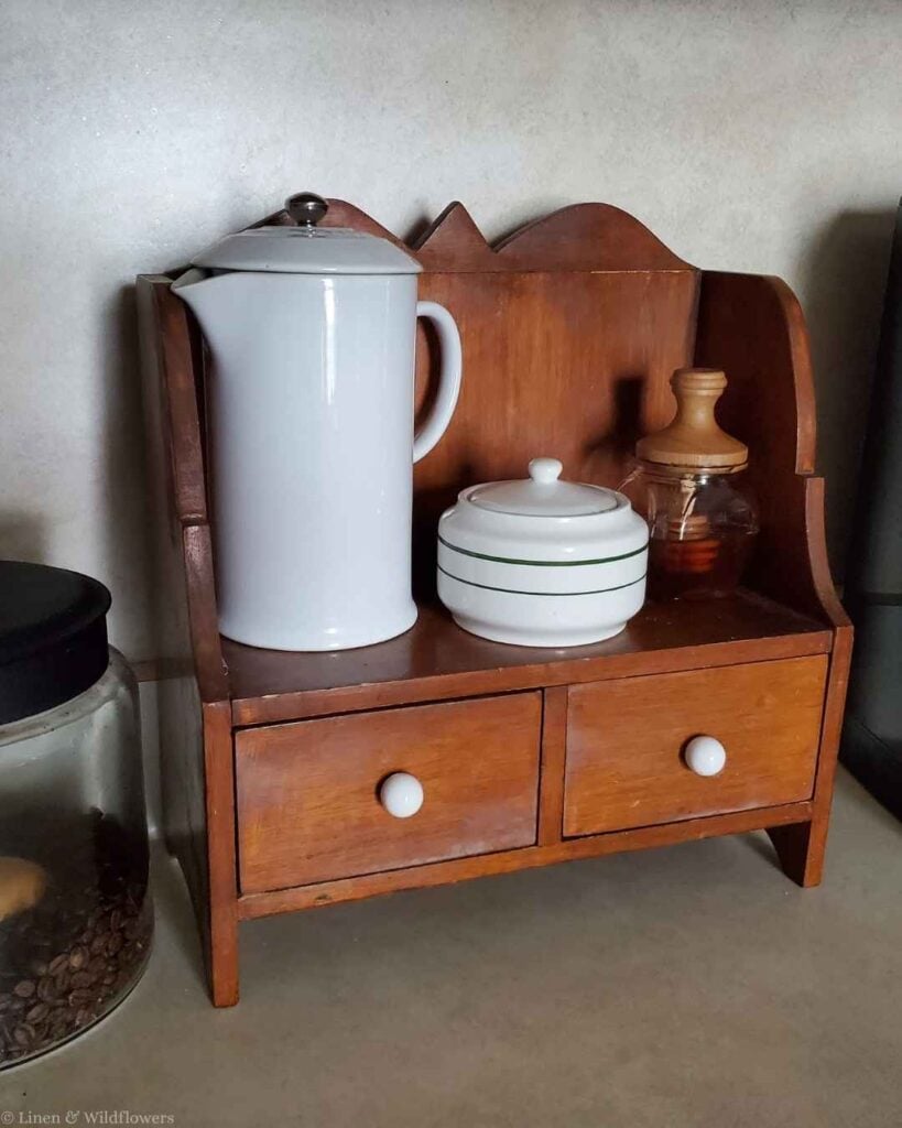 Small honey jar displayed on a vintage two-drawer wood shelf with a white pitcher and covered sugar bowl.