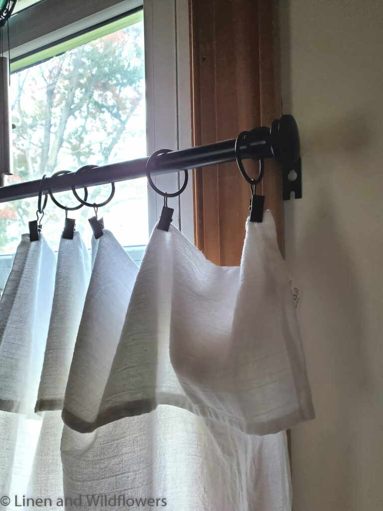 No Sew Tea Towel Curtains hanging from black ring curtain clips on a black rod on the window.