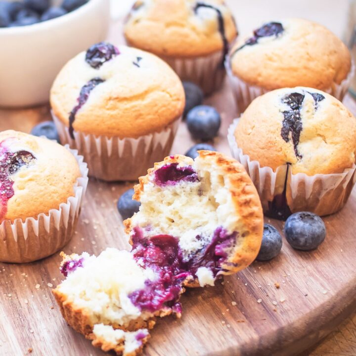 A batch freshly made Easy Recipe for Bisquick Blueberry Muffins out of the oven, A muffin already pulled apart ready tp dig in.
