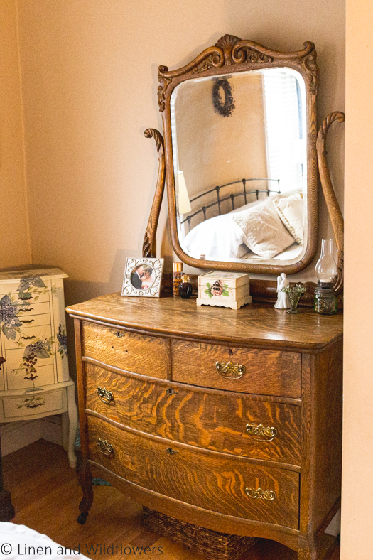 Victorian tigerwood Dresser in a master bedroom. In the corner of the room is a floral painted standing jewelry box. 