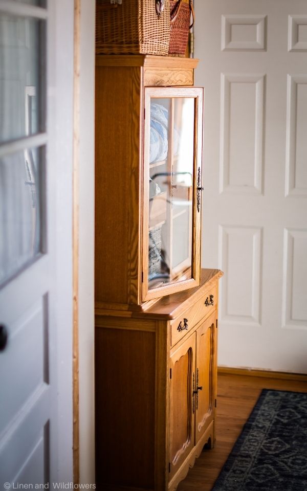An antique stepback cupboard that is made with maple wood from 1910-1920 with the glass door of the cabinet opened.