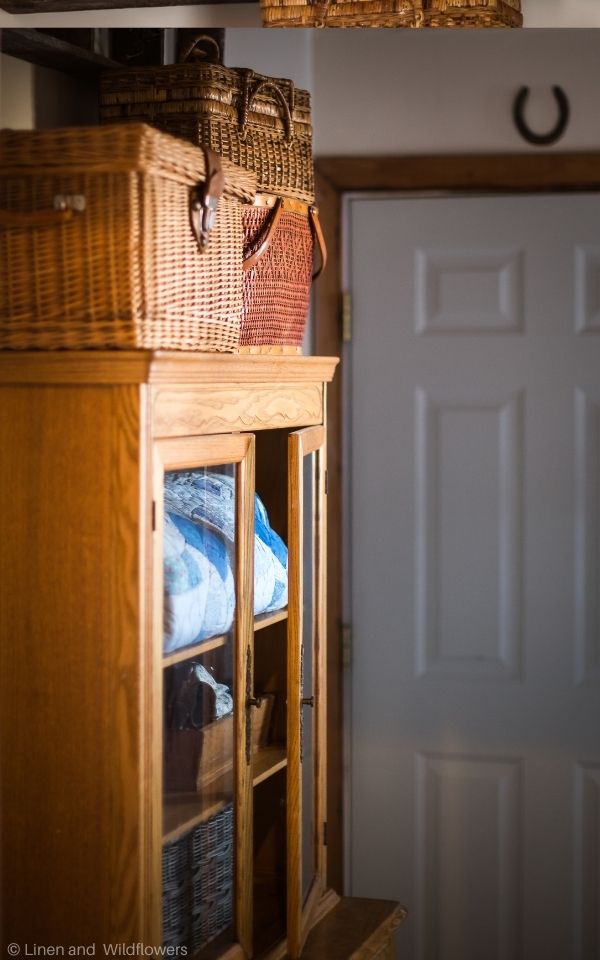 An antique stepback cupboard that is made with maple wood from 1910-1920 with vintage basket on top and inside is a quilt with blue & flower patterns, along with a tool caddy & basket.