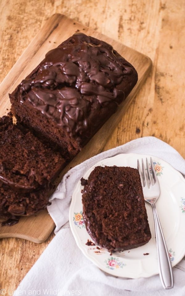 A plate with a slice of triple chocolate banana bread & fork next to a cutting board with a loaf of triple chocolate bread.