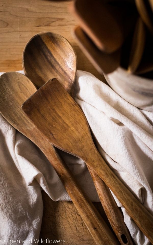 16 Useful Kitchen Tips-wooden utensils on a tea towel next to a crock of wooden utensils.