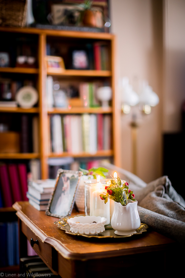 a sofa table with décor books, a wedding photo, a plant in a milk glass planter & a gold tray with a milk glass bowl with skeleton keys, a iron creamer pitcher with mini fake roses & a candle holder with 3 pillar candles kit.