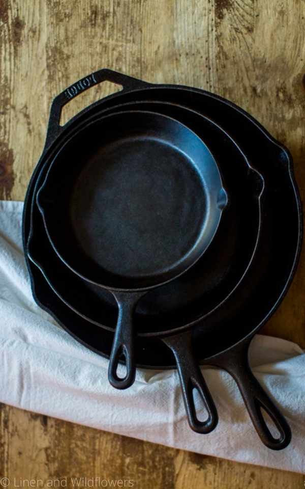 3 different sizes of cast iron skillet next to a tea towel.