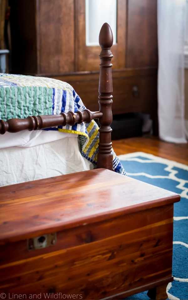 a vintage blanket chest at the foot of a antique spindle bed frame.