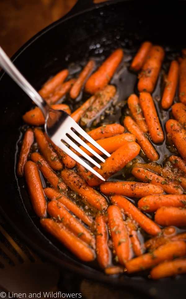  A lodge cast iron skillet with honey glazed carrots and a fork with a carrot.
