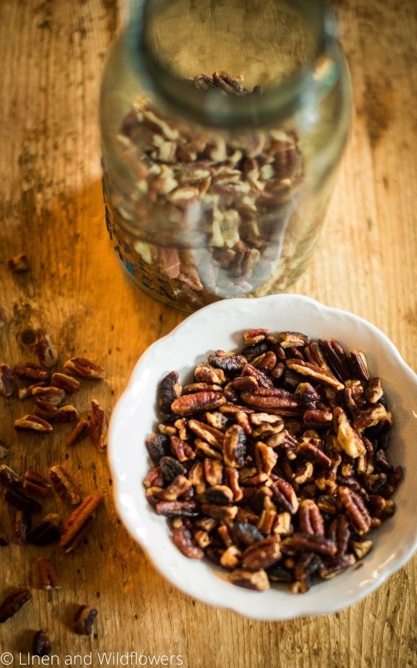 Delicious roasted pecans in a bowl next to a mason jar with pecans & some on the table. This is another easy snack on the 5 easy & quick snack recipes list.