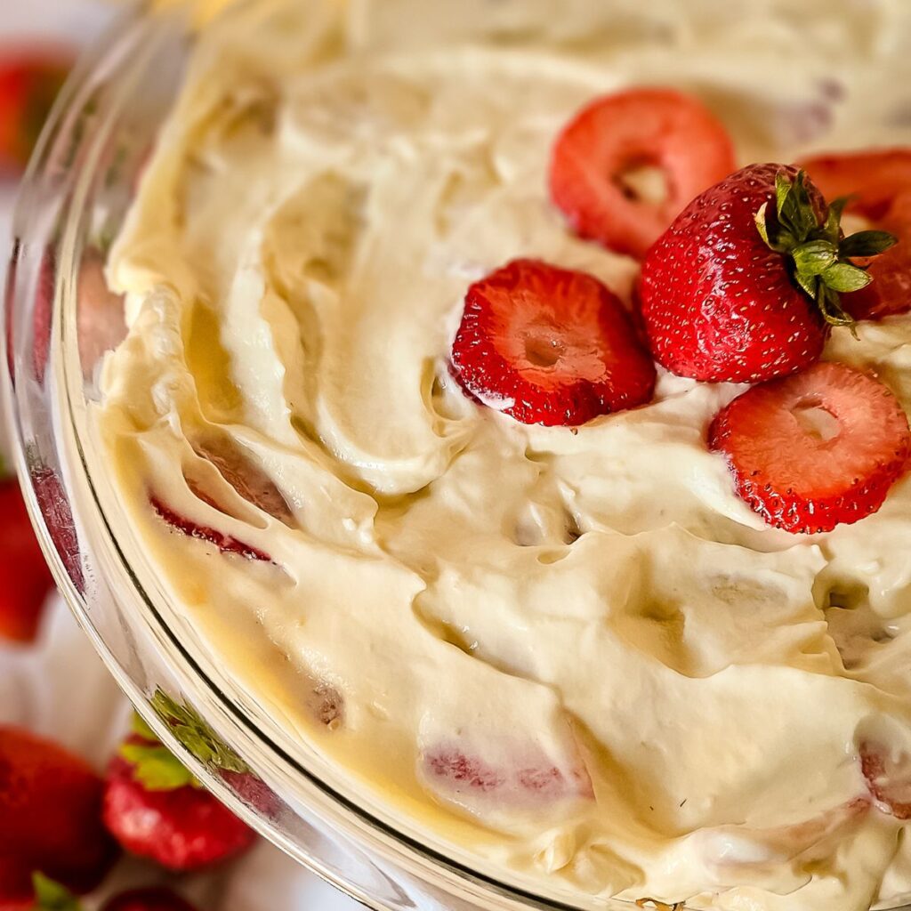 Creamy dessert topped with fresh, sliced strawberries in a glass dish, evoking a sweet, inviting tone. Smooth texture with vibrant red accents.