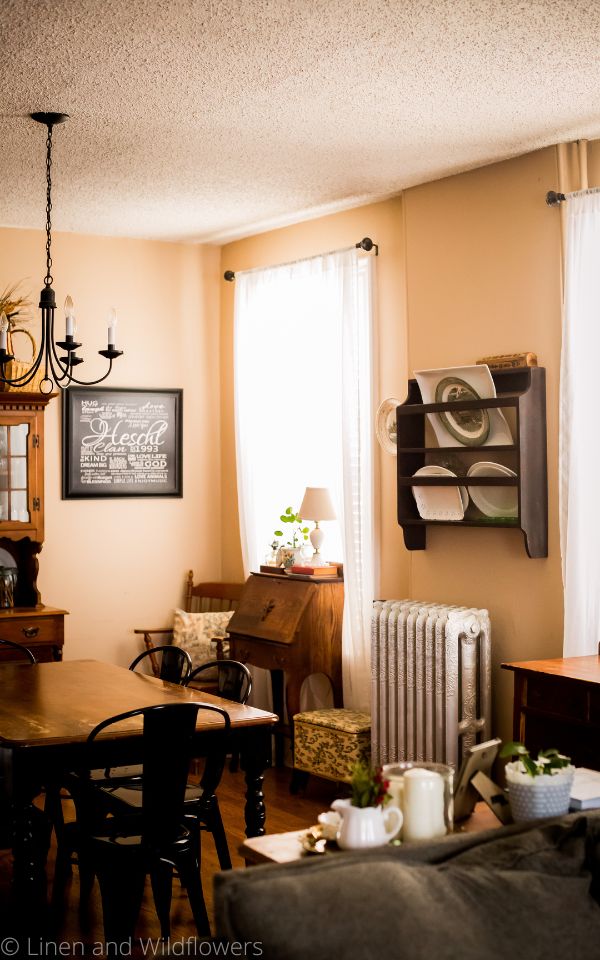 A dining room decorated in a mix of American Country, Farmhouse & English cottage style with thrifted finds & antiques. On the wall is a plate rack that holds platters. Under the rack i a cast iron radiator original to the 1885 house.