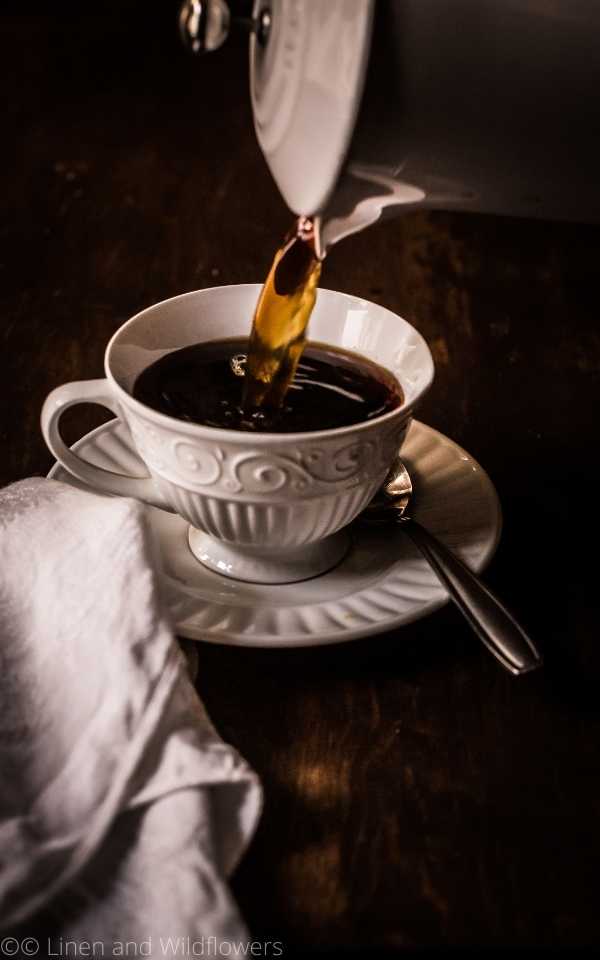 Pouring a cup of coffee from a French press. The little details of a linen napkin, china cup & saucer on a wood table.
