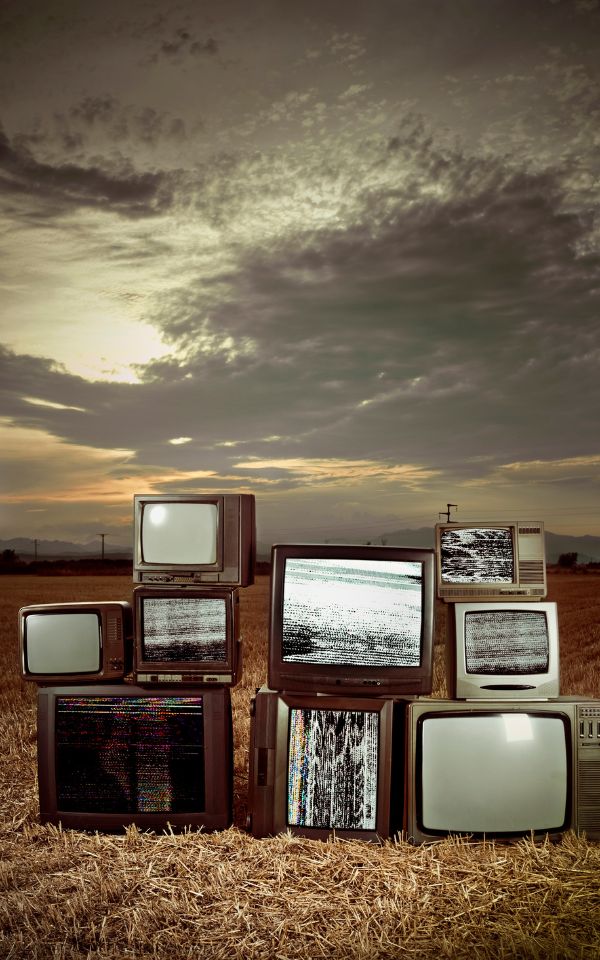  A variety of vintage televisions stacked in a cloudy dessert