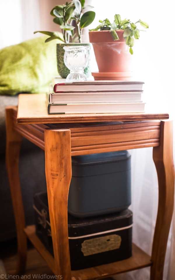 Unique Vintage Swivel Top Table serves as a end table that can swivel out that holds a lamp, books stacked with a candle holder & two plants in front of a window.