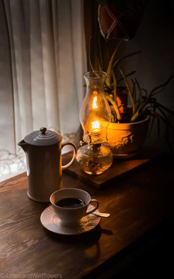 How to decorate with oil lamps is a beautiful way to create an ambiance feel in the space. A French pot, coffee cup on saucer with a spoon, a aloe plan sitting by a lit oil lamp in the earl morning.