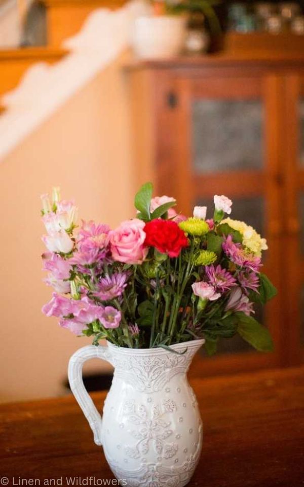  A white pitcher wit an assorted arrangement of flowers.