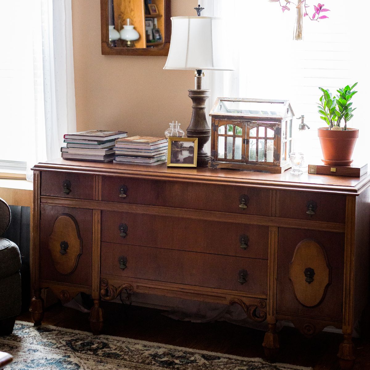 5 Uses for an Antique Sideboard-LinenandWildflowers.com | A sideboard styled with a lamp, stacks of decor books. terraium with house plants, a small oil lamp, candle & a plant resting on a old cigar box.