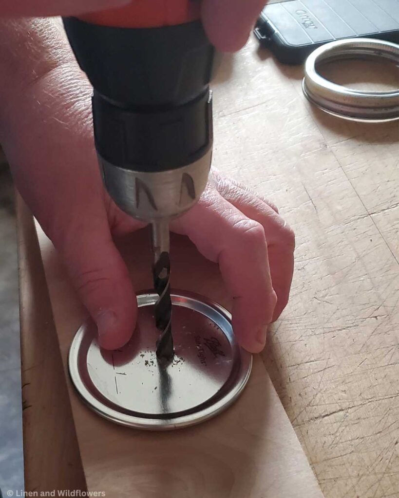 A man drilling a hole in the center of a mason jar seal for a diy project.