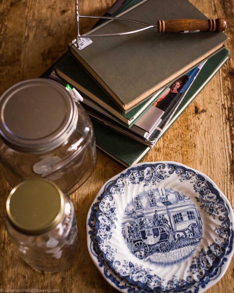Thrift finds for Home Decor, a stack of books, potato masher with a wood handle, 2 glass jars & 2 blue & white ironstone plates.