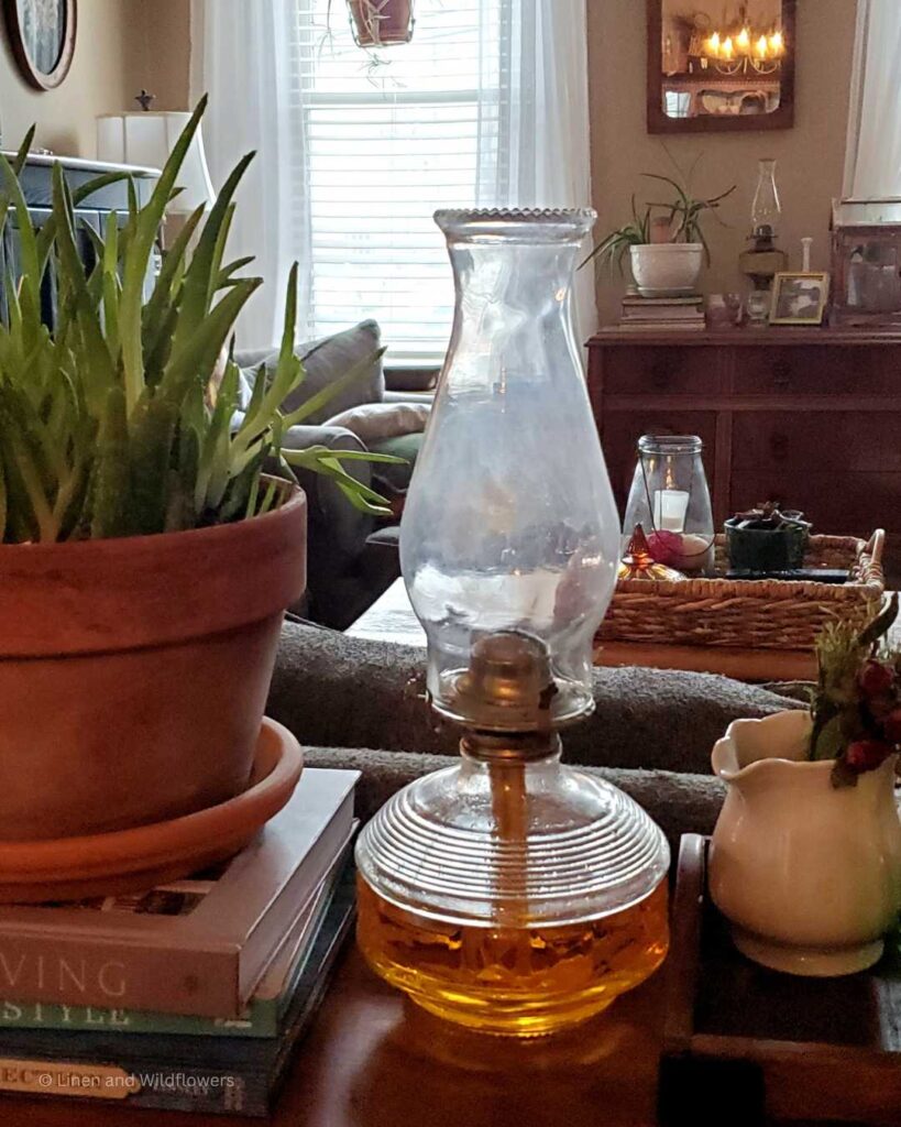 An oil lamp on a table with home decor surrounding it on a table.