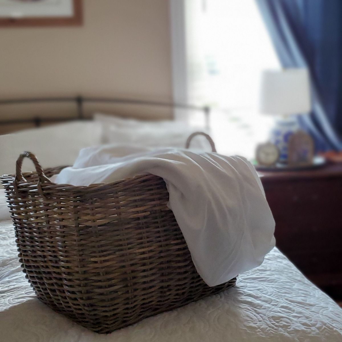 A wicker basket of white linens on top of a freshly made bed.