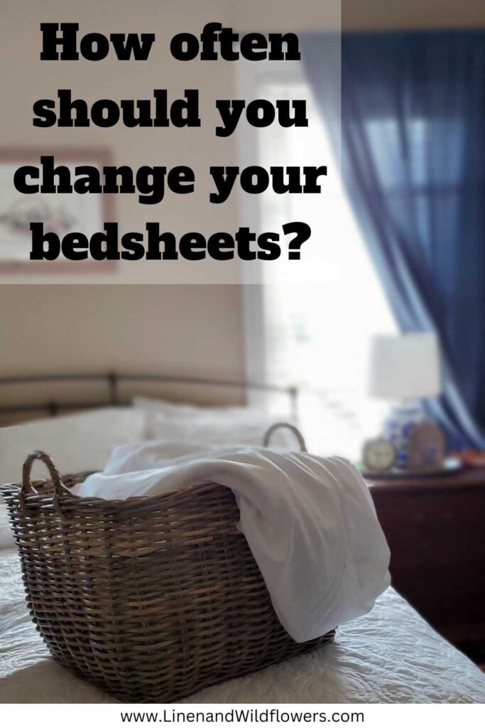 A Pinterest Pin for How often should you change your bedsheets- A wicker basket of white linens on top of a freshly made bed.