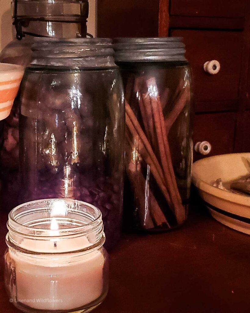 A small candle in a mason jar with two antique mason jars behind it filled with coffee beans & cinnamon sticks.