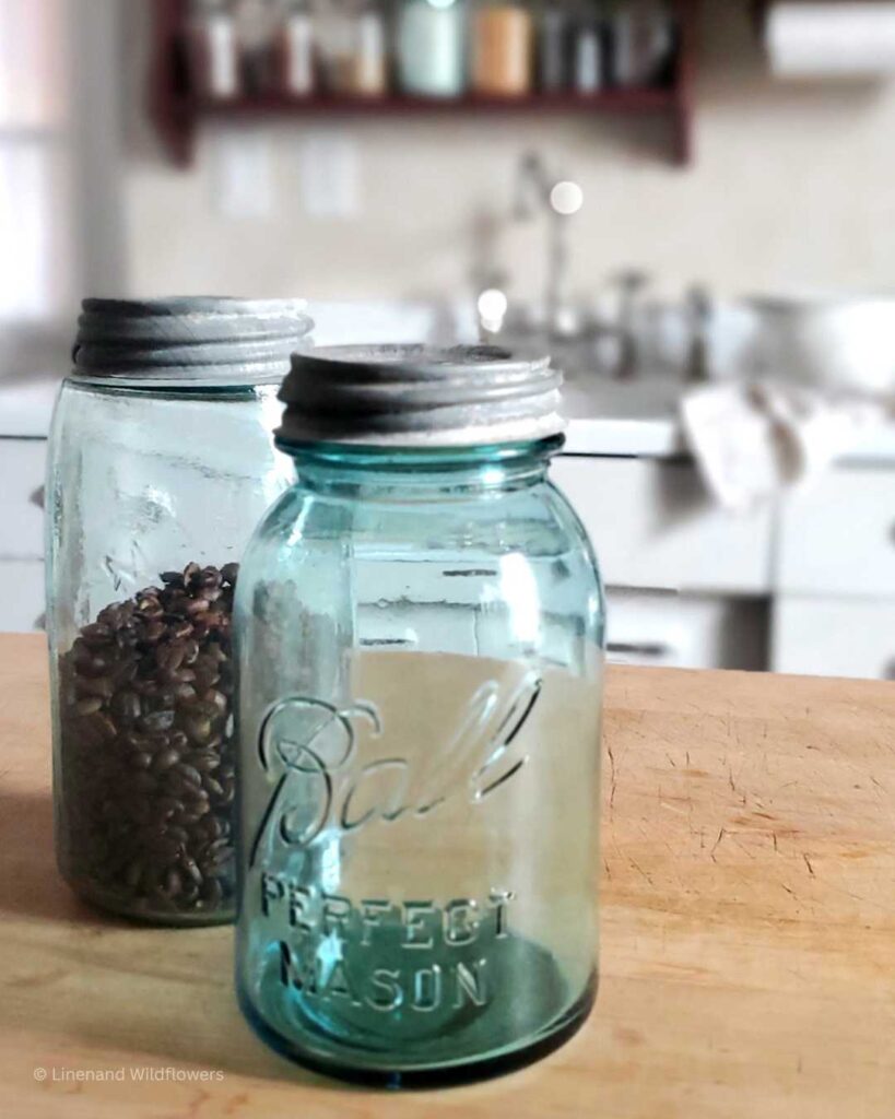 two antique mason jars on a butcher block in front of a vintage sink with a two tiered shelf filled with antique mason jars.