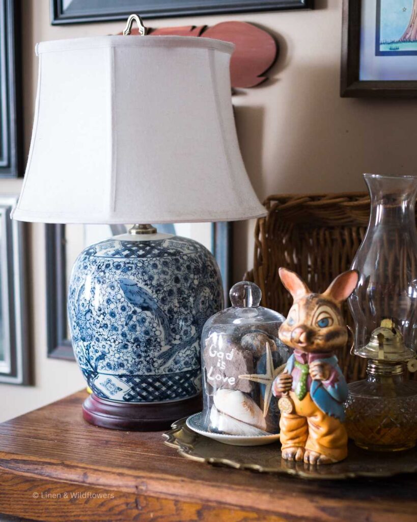 A oriental lamp,  cloche filled with sea shells & a rock that that says "God is Love", a handmade ceramic Easter bunny & an oil lamp.