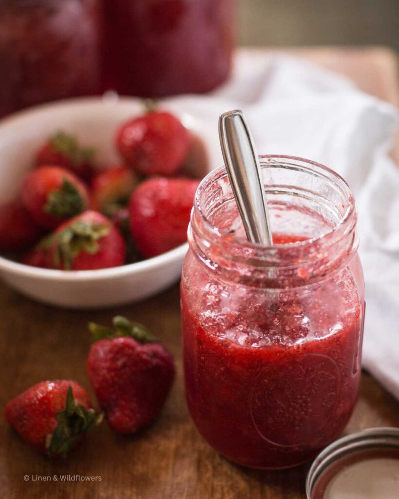 A mason jar filled with homemade strawberry jam & a bowl of fresh straberries.