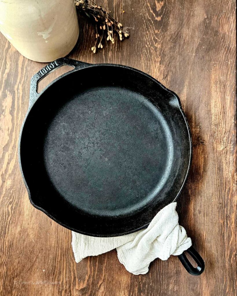 A cast iron skillet with a linen towel wrapped around the hot skillet handle on a wood table.