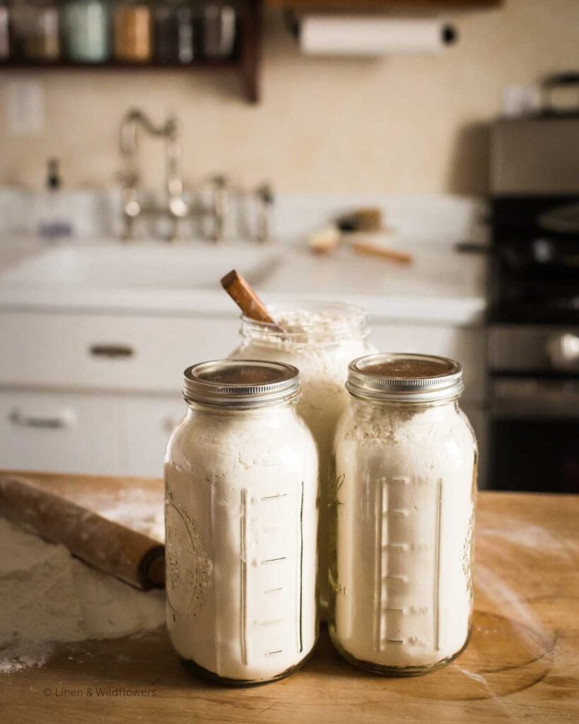 Three jars of flour equaling 10lbs of flour on a butcher block in front a vintage sink.