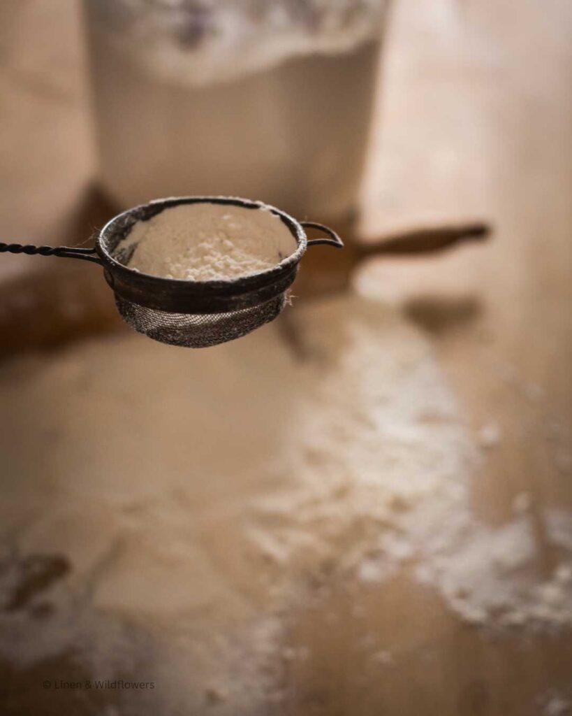 Flour being sifted through a antique handheld sifter.