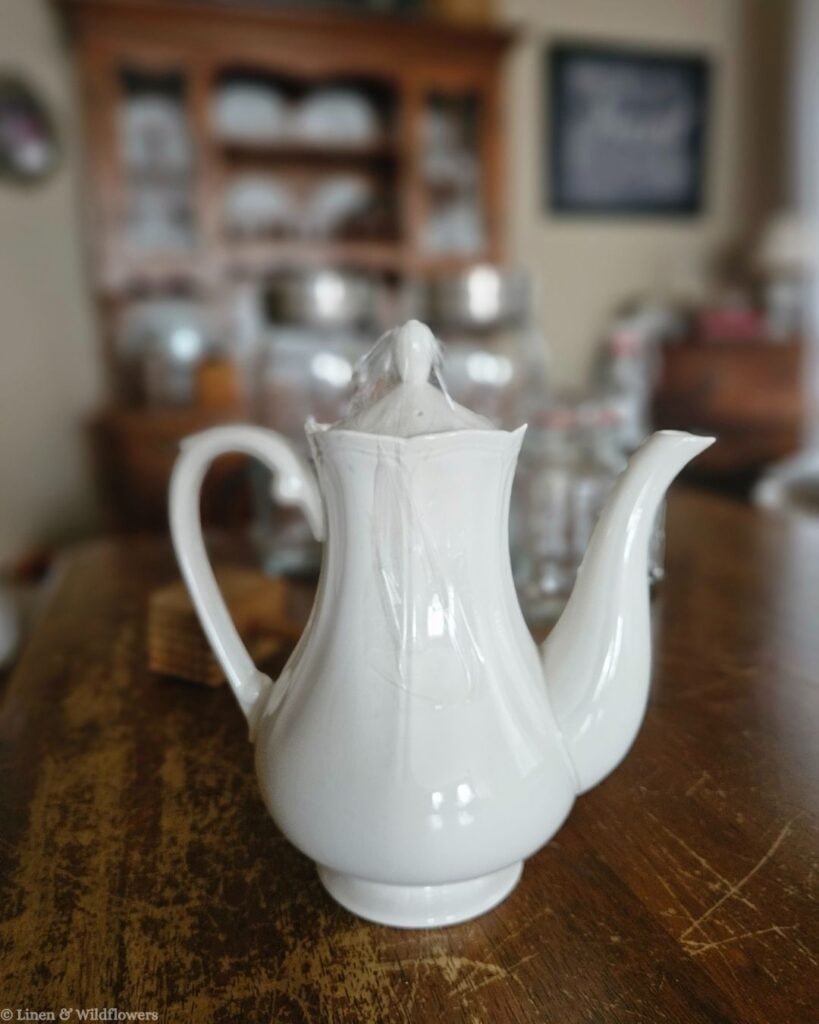 Close-up of an antique white ironstone coffee pot, a classic thrifted piece for farmhouse and cottage-style shelves.
