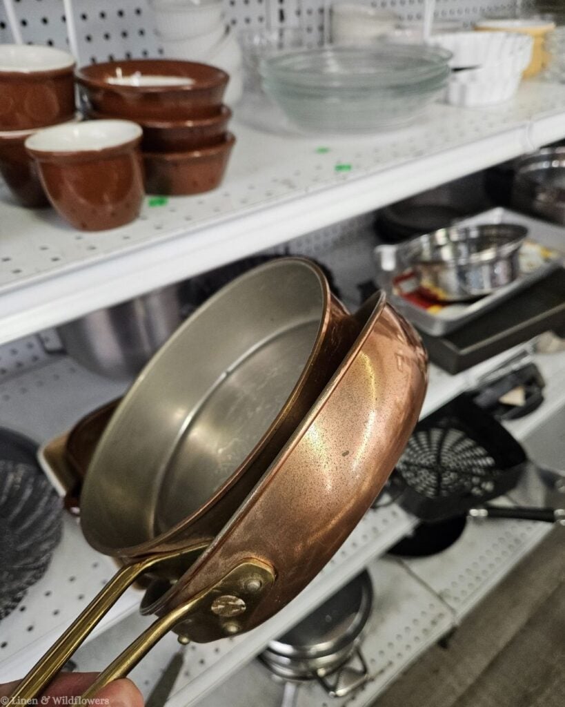 Hand holding thrifted copper-bottom pots and pans discovered while antiquing, great vintage cookware for display or use.
