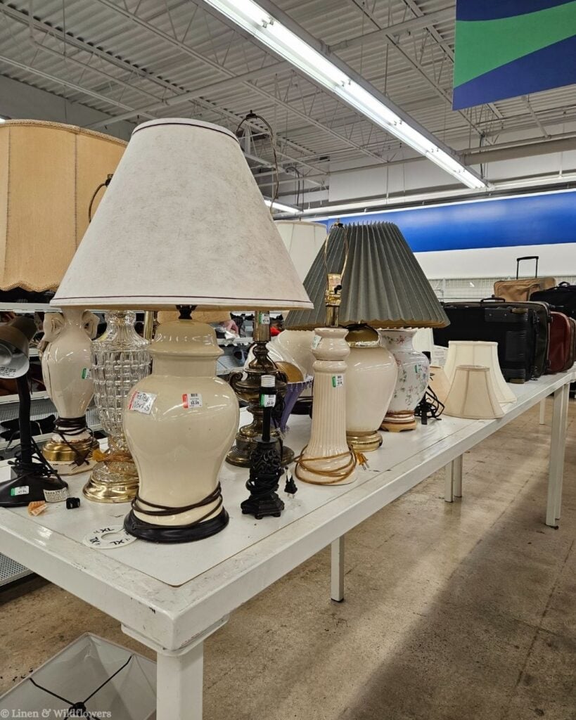 Row of vintage ceramic ginger jar and brass lamps lined up on a thrift store table, ideal for intentional home lighting.