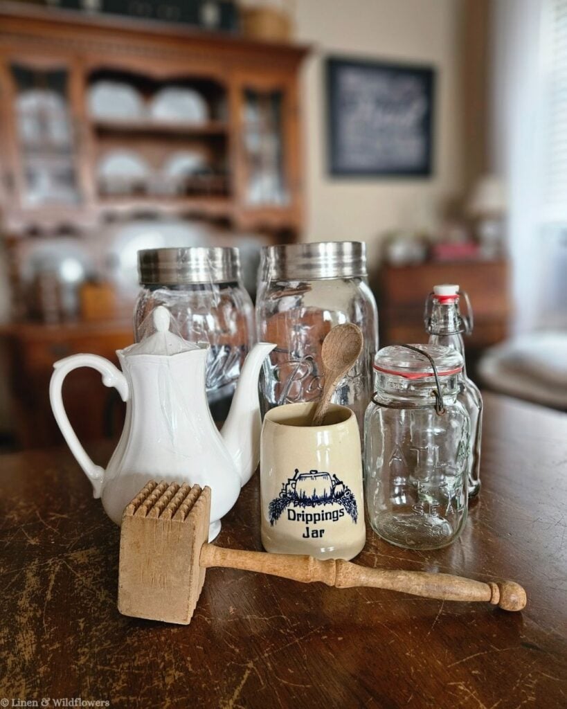 Vintage ironstone teapot, Ball mason jars, and a stoneware drippings jar styled on a farmhouse kitchen table for cozy décor.