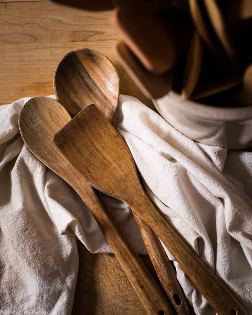 Close-up of a clean wooden spoon and spatula resting on a linen towel after washing.