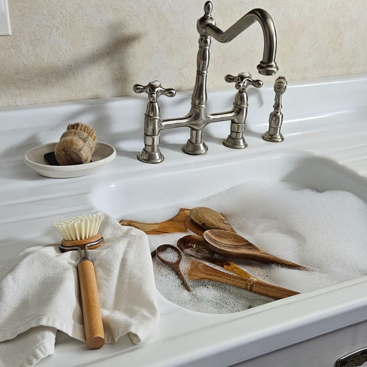 How to clean and sanitize wood utensils — wooden spoons soaking in soapy water at a farmhouse sink.