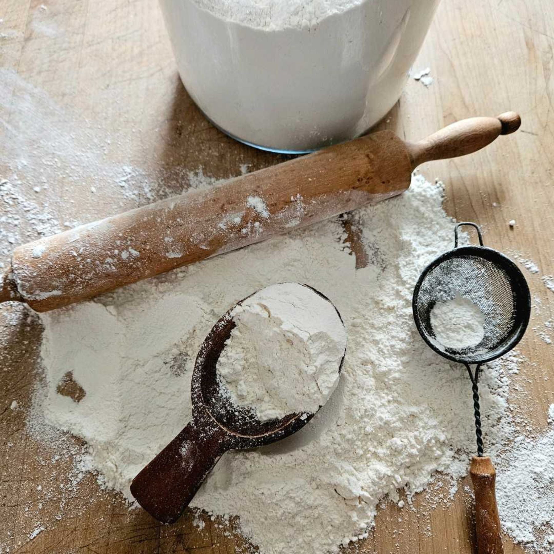 Flat lay of flour, a wooden rolling pin, measuring scoop, and sifter, the feature image for 46 useful kitchen and cooking tips and hacks.