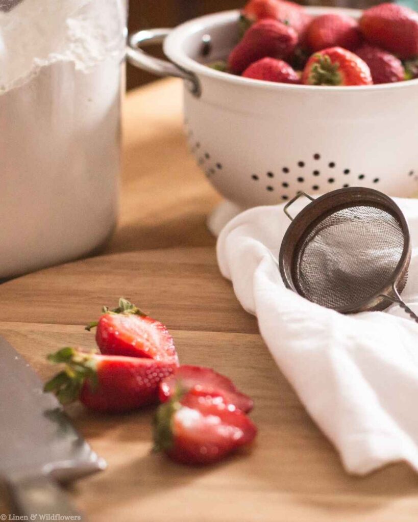 Sliced fresh strawberries beside sifted flour and a colander, a simple baking prep tip for homemade desserts.