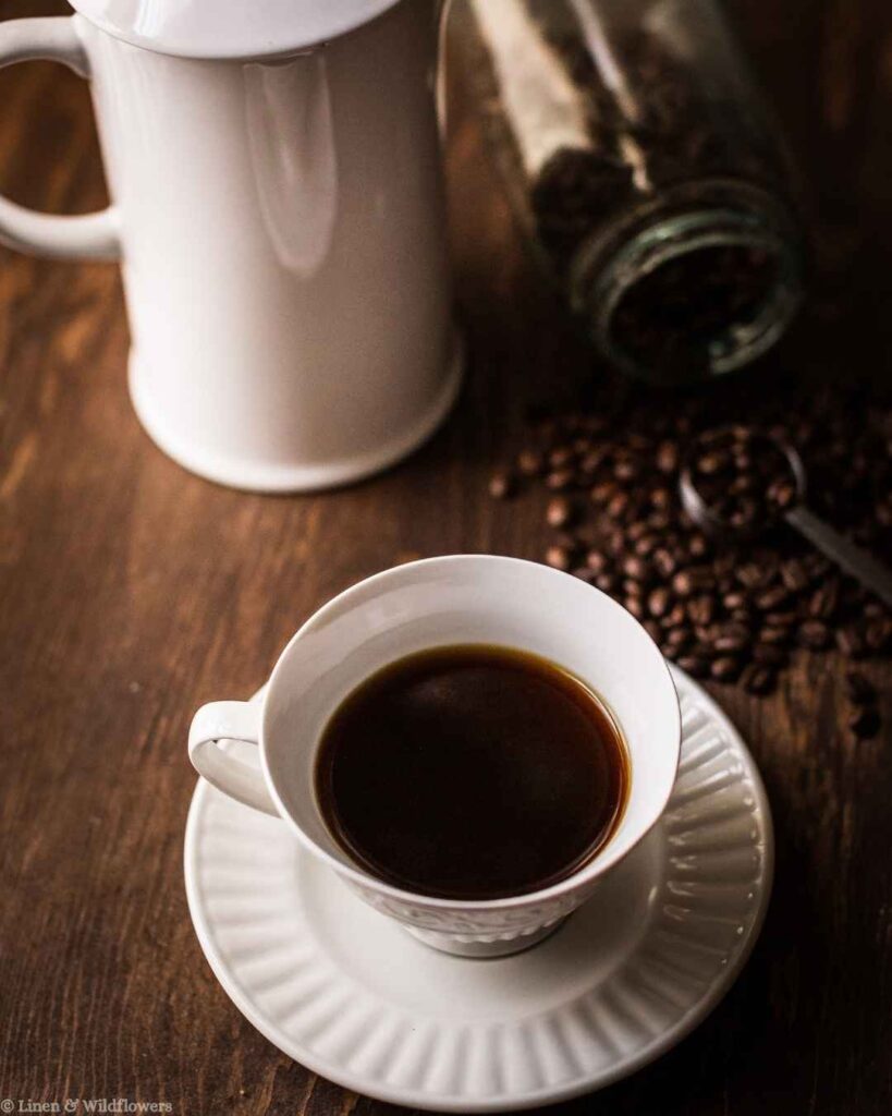 A cup of fresh brewed coffee in a vintage teacup with whole coffee beans, a simple morning coffee hack.