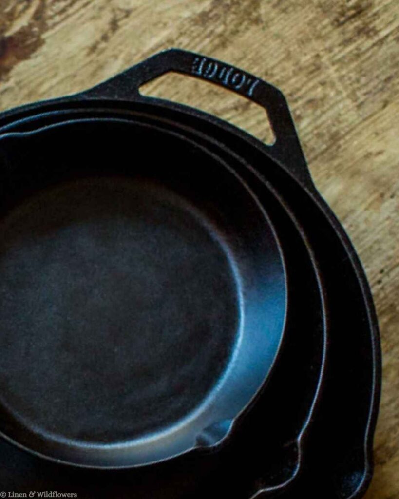 Stacked Lodge cast iron skillets on a wooden countertop, a simple storage tip for organizing cast iron cookware.